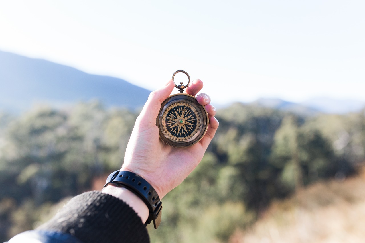 An outstretched hand holding onto a navigation compass in a rustic outdoor setting