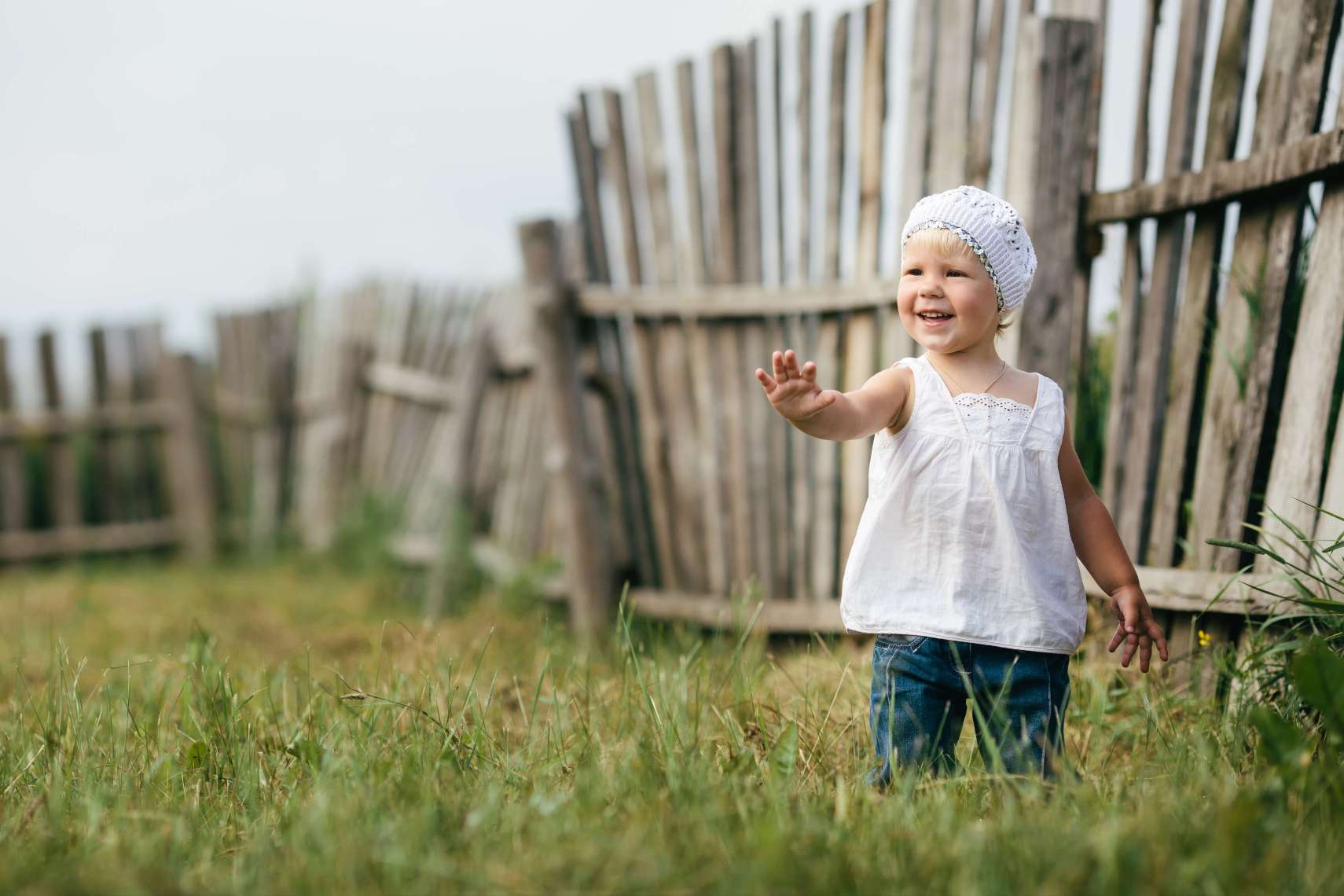 Young girl in a knitted hat standing in front of a fence and holding out her hand in a STOP gesture